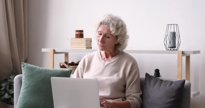 Inspired thoughtful older lady typing on laptop at home. Elderly 70 years old adult woman using computer thinking of new ideas sit on sofa. Senior female user writing internet blog social media post