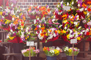 Fototapeta na wymiar Flower market with many bouquets on display at spring over brick red wall
