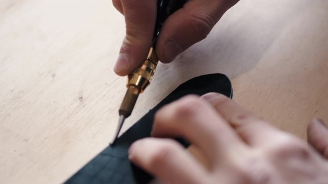A leather craftsman is cutting the edges of a belt. The master is using an edge beveler tool.