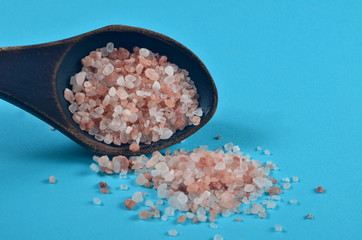 Fototapeta na wymiar Himalayan pink salt in dark wooden spoon on blue background