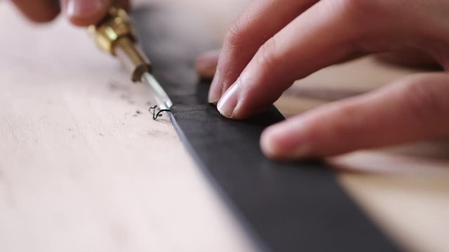 A leather craftsman is cutting the edges of a belt. The master is using an edge beveler tool.
