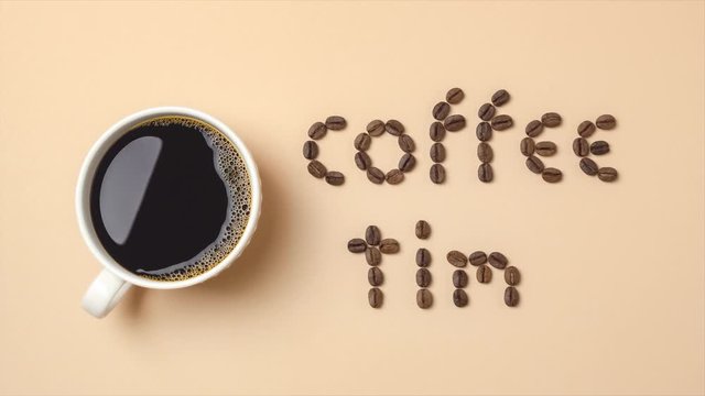 Top view of stop motion roasted coffee beans arranged in letters and hot coffee in white coffee cup on light brown background for coffee menus or coffee shop signs. 4K resolution ultra HD.