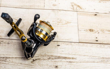 Golden fishing reel on wooden floor, equipment with pe line, rust-proof technology, ball bearing system - Powered by Adobe