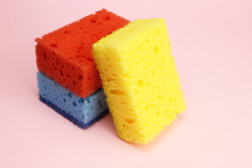 Colored sponges for dishes or home cleaning on a pink background