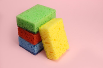 Colored sponges for dishes or home cleaning on a pink background