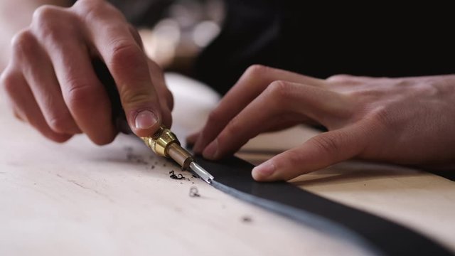 A leather craftsman is cutting the edges of a belt. The master is using an edge beveler tool.