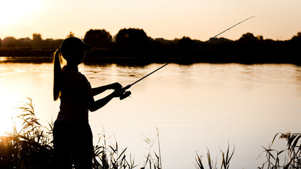 Silhouette of a young girl with a fishing rod on the river Bank
