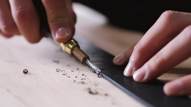 A leather craftsman is cutting the edges of a belt. The master is using an edge beveler tool.