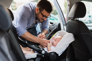 Young father putting his baby boy on a safety child car seat.
