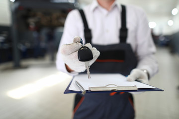 Close-up view of service station worker returning keys to owner and filling clipboard paper. Car...