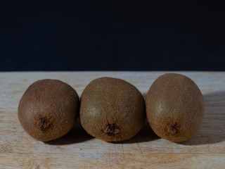 Three whole kiwis lined up on a wood