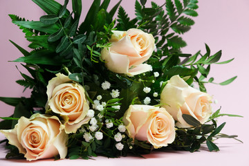 Beautiful fresh blooming bouquet of pink roses and gypsophila with green leaves of fern on a pink...