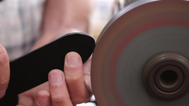 A craftsman is sharpening the edges of a belt on a special machine. The leather master is making a men's leather belt manually.