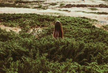 Depressed girl with long hair standing in green grass