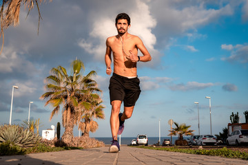 joven  con el torso desnudo sale a correr a la calle a última hora de la tarde