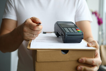 Close-up view of man holding cardboard box and payment terminal in hands. Credit card contactless...