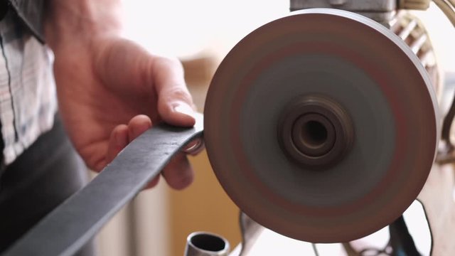 A craftsman is sharpening the edges of a belt on a special machine. The leather master is making a men's leather belt manually.