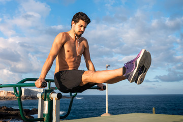 joven atleta levanta las piernas y se mantiene en el aire, usando un aparato de gimnasio público...