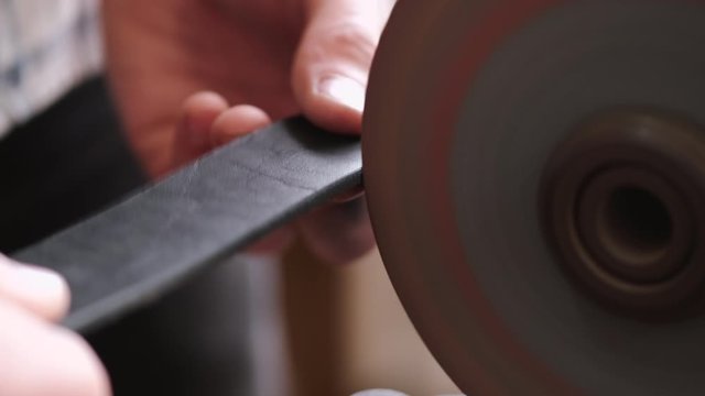 A craftsman is sharpening the edges of a belt on a special machine. The leather master is making a men's leather belt manually.