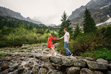 Naklejka premium a young couple, a girl in a red dress, and a man in a white T-shirt and blue pants, are walking in the Tatra National Park in Poland