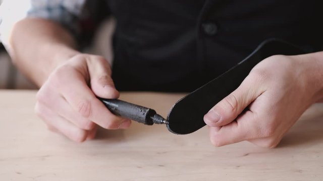 A leather master is dying leather belt edges. A craftsman is making hand-made men's leather belt.