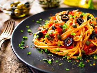 Pasta puttanesca with tomato sauce, anchovies, chilli, capers and olives on wooden table