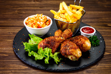 Roast chicken drumsticks with french fries on black stone board