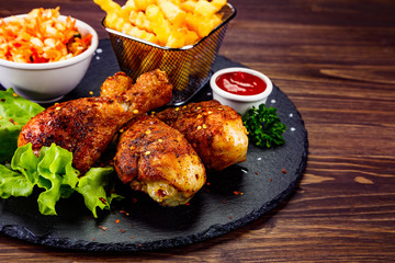 Roast chicken drumsticks with french fries on black stone board