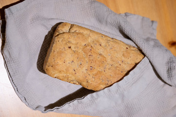 Frisches selbstgebackenes brot aus einer kastenform leigt eingehüllt in ein graues tuch auf einem...
