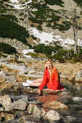 young girl in a red dress sits near a stream in the Tatra National Park in Poland