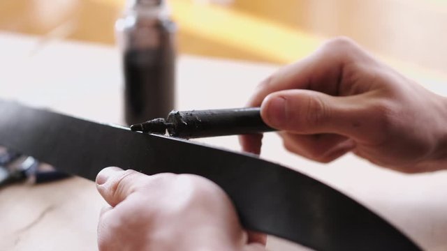 A leather master is dying leather belt edges. A craftsman is making hand-made men's leather belt.