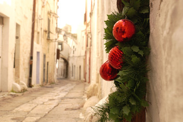 Small stone street with white buildings and preserved Christmas green decoration with red balls in...
