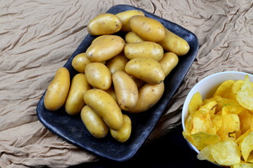 Small washed potatoes and potato chips on a fabric background. View from above. Raw potato food