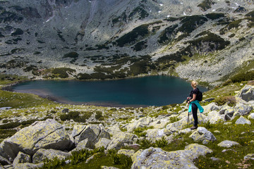 Naklejka premium Young hiker woman standing on the lakeside, Retezat mountain range, Romania. Freedom and beauty in nature