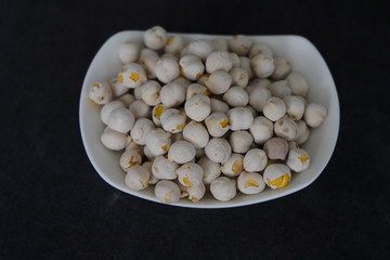 White chickpeas in bowl on black background.
