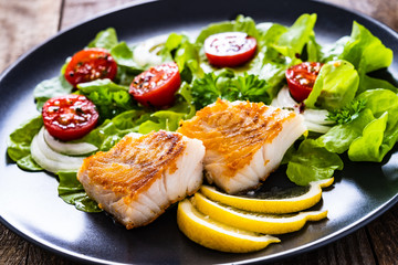 Fish dish - fried cod fillet with vegetables on wooden table