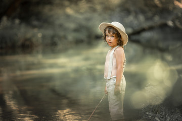 A boy in trousers and without shirts near rivers in the forest with wand in the hands of as if fisherman