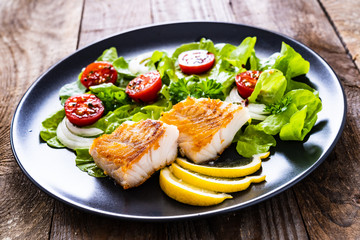 Fish dish - fried cod fillet with vegetables on wooden table