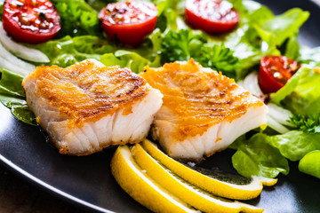 Fish dish - fried cod fillet with vegetables on wooden table