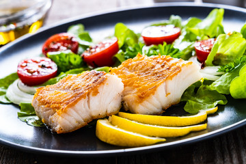 Fish dish - fried cod fillet with vegetables on wooden table