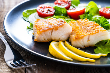 Fish dish - fried cod fillet with vegetables on wooden table