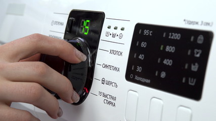 A young woman turns on a washing machine. A woman turns the lever choosing the mode on the washing machine. Hand close-up.