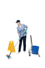 Girl in a cleaning uniform with a mop and a bucket on wheels, isolated on white background and a wet floor sign