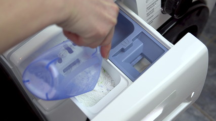 A young woman pours detergent into a washing machine. A woman fills powder and pours liquid into a special compartment in the washing machine. Hand close-up.