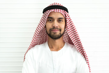Portrait of happy smiling handsome middle eastern arab man in traditional clothing standing on white wall background