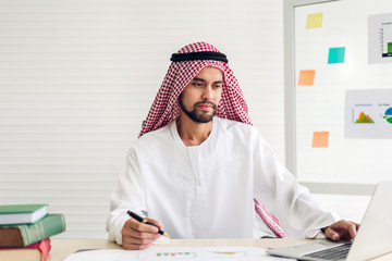 Handsome confident arab businessman working and looking at technology of laptop computer monitor.Creative coworkers arabic business people write on document report and planning at modern work loft