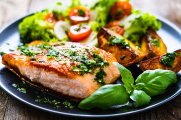 Fried salmon steak with potatoes and vegetables on wooden table