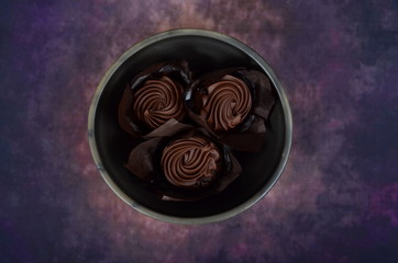 Three chocolate muffins in a clay bowl on a colored background