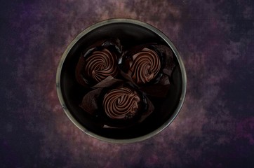 Three chocolate muffins in a clay bowl on a colored background