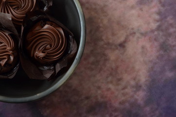 Three chocolate muffins in a clay bowl on a colored background
